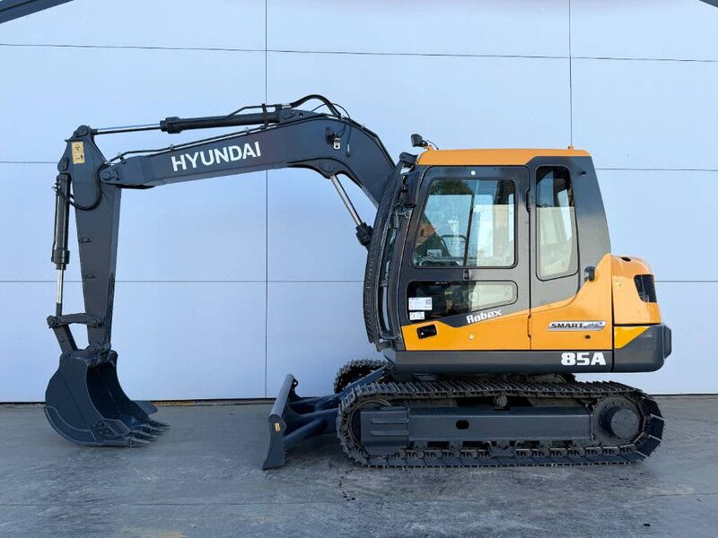 2026 Hyundai R85A Crawler Excavator with its orange body and dark gray boom extended to the left, showing the digging bucket. 2026 Hyundai R85A Crawler Excavator with its orange body and dark gray boom extended to the left, showing the digging bucket.